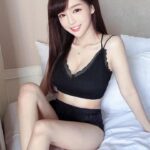 KL Escort Girl Smiling Asian woman in black lingerie set sitting on a bed with white sheets. Malaysia Sex Service