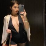 KL Escort Girl Woman in a black romper taking a mirror selfie with a pink purse and white jacket. Malaysia Sex Service