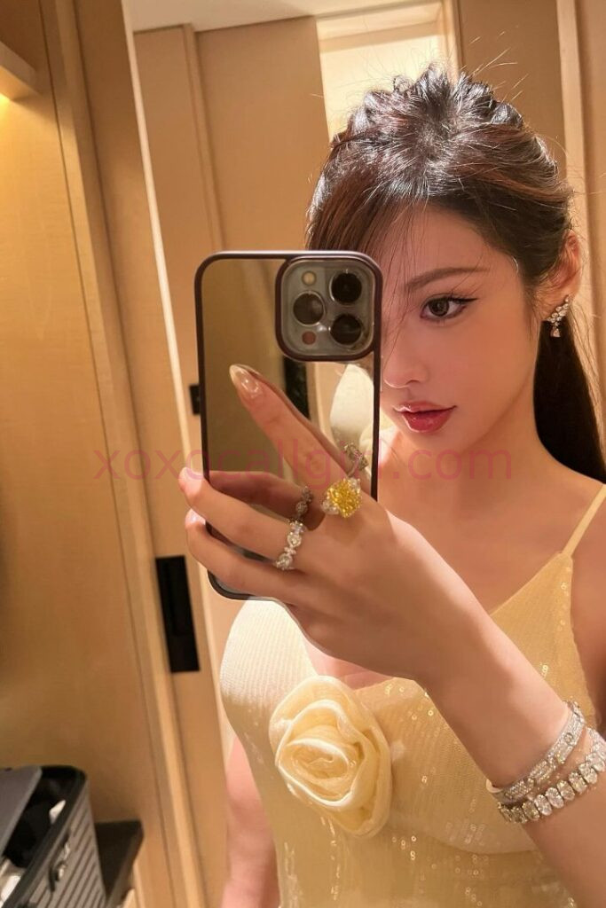 KL Escort Girl Woman in gold lingerie sits on a bed, smiling. Bedroom setting. Malaysia Sex Service