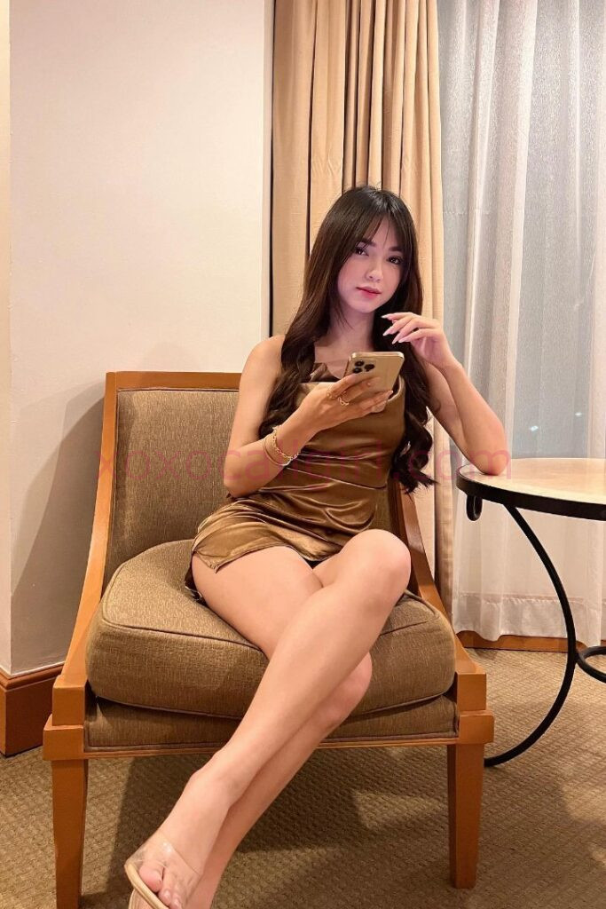 KL Escort Girl Malay Escort in Kuala Lumpur sits in a chair using her phone. Malaysia Sex Service
