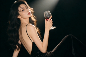 Elegant woman in black dress holding red wine glass.